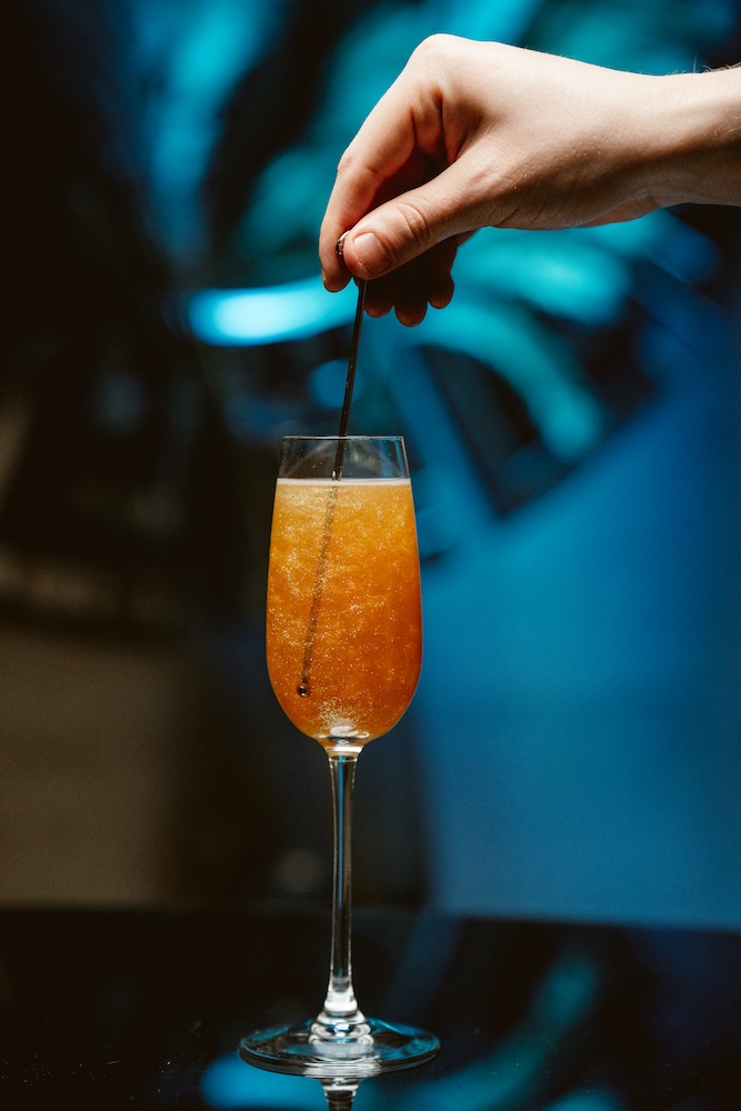a hand holding a straw in a glass of orange liquid